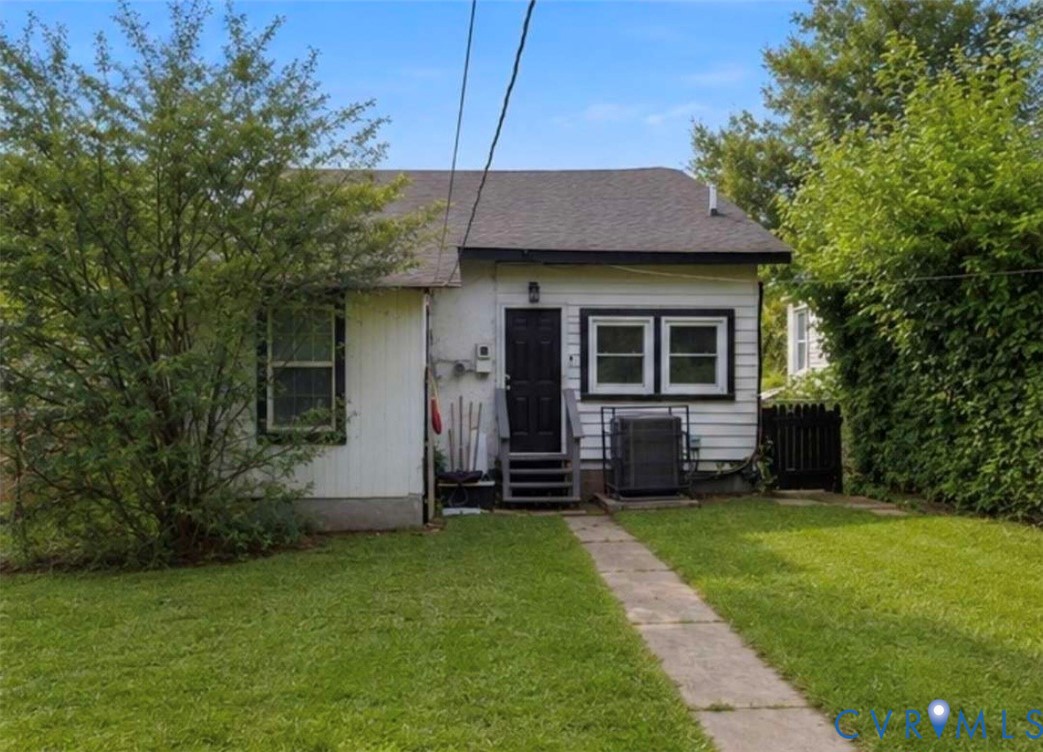 Rear exterior featuring white siding with dark trim, a dark rear entry door, and a concrete pathway through the lawn