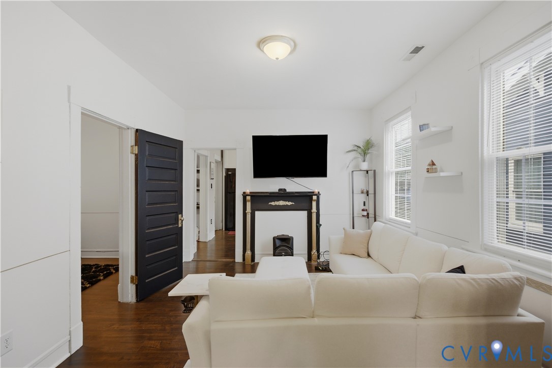 Living area featuring rich wood-finish flooring and multiple windows with blinds