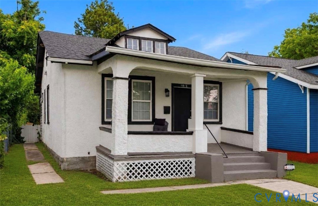 White stucco exterior featuring a covered porch with arched supports, dark trim accents, a black front door, and a dormer window White stucco exterior featuring a covered porch with arched supports, dark trim accents, a black front door, and a dormer window