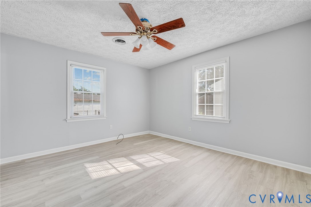 Wood-finish flooring, two windows with white trim, and a ceiling fan with light fixture