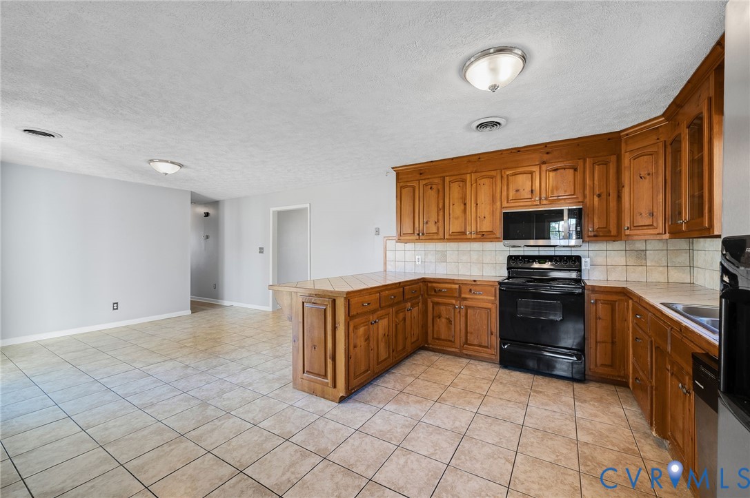 Kitchen featuring wood cabinetry, black appliances, tile flooring, and tile countertops
