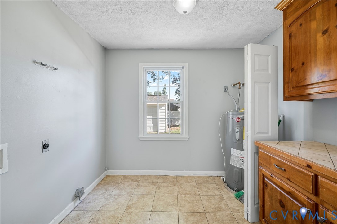 Room featuring neutral wall tones, tile flooring, window with white trim, wood-finish cabinetry, and a tile countertop