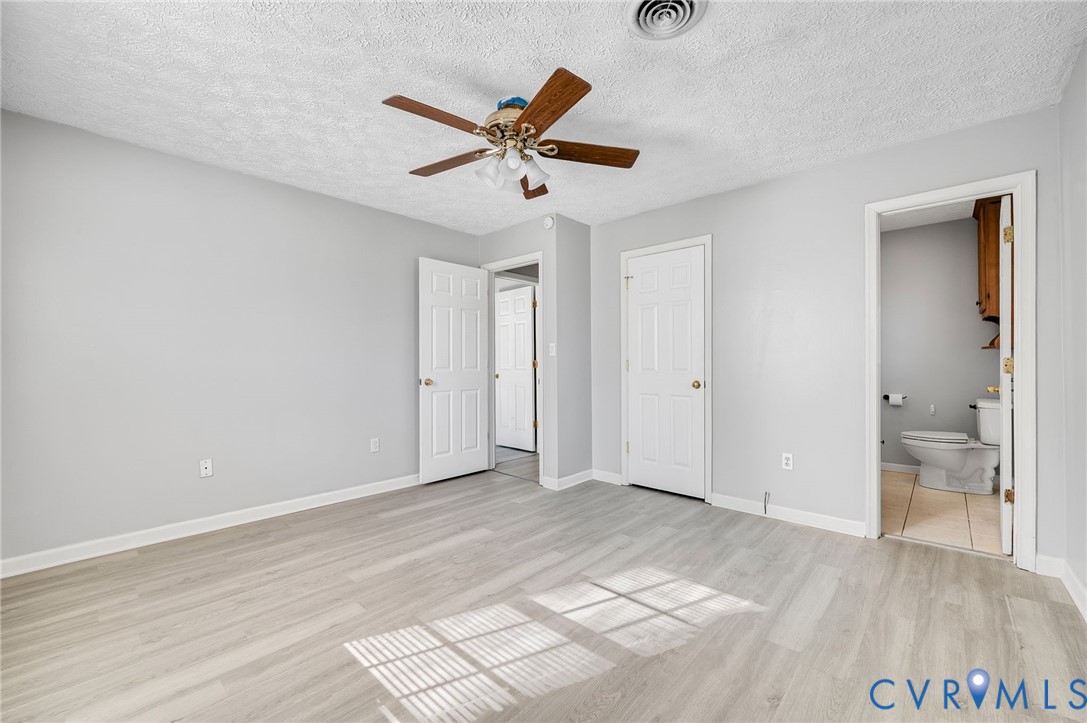 Neutral wall paint, wood-finish flooring, ceiling fan with light fixture, paneled doors, and a private water closet