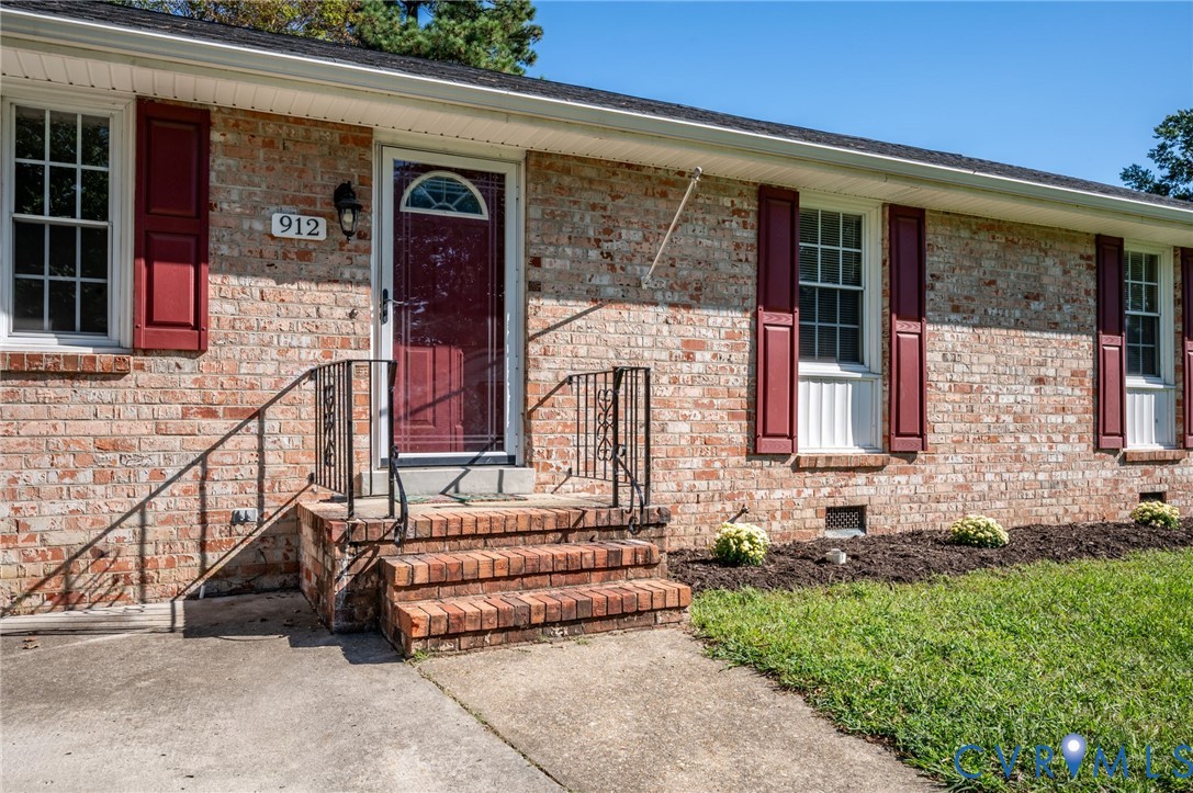 Brick exterior with red shutters, a red front door, and a traditional brick stoop with wrought iron railings