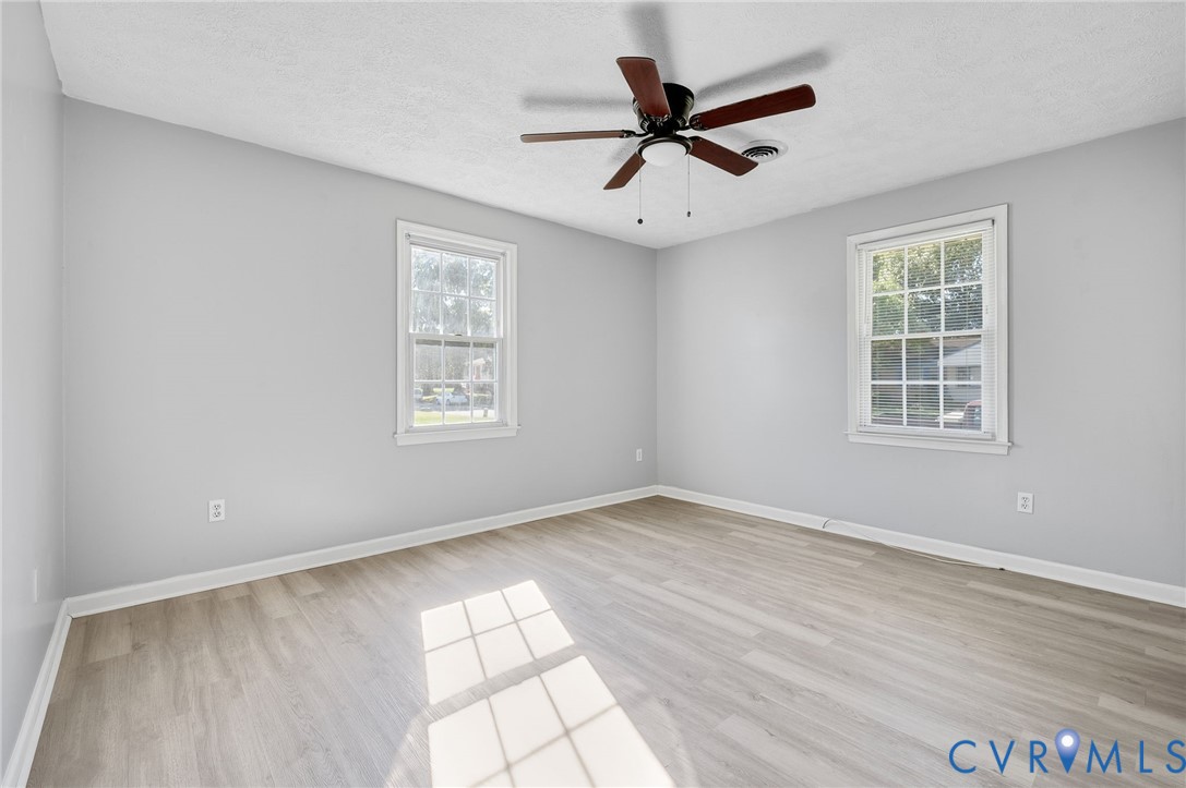 Wood-finish flooring with light gray walls, two windows, and a ceiling fan with integrated lighting