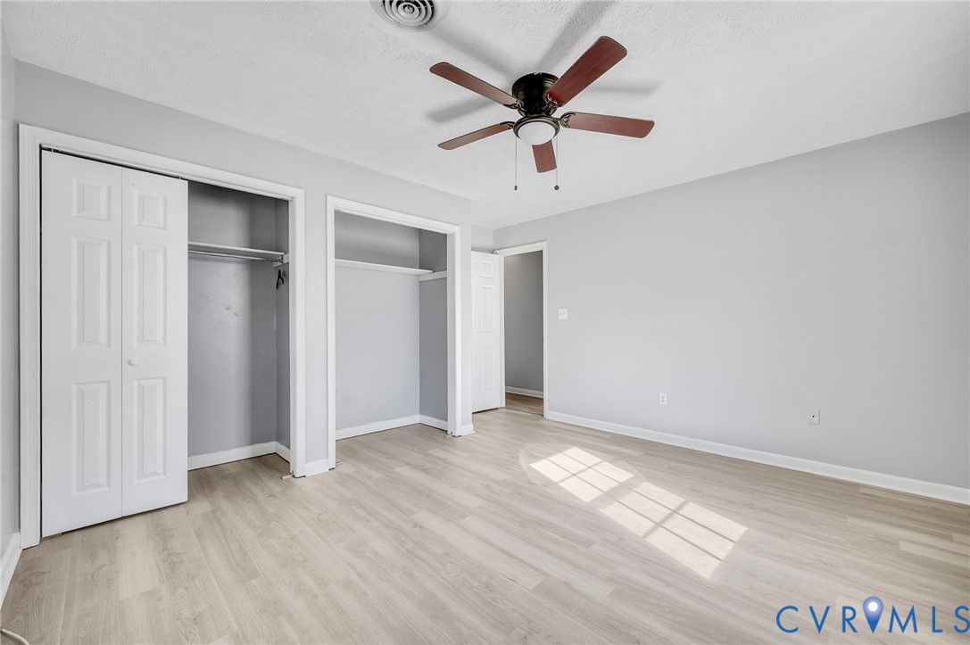 Wood-finish flooring, ceiling fan with light fixture, light gray wall tones, and bi-fold closet doors