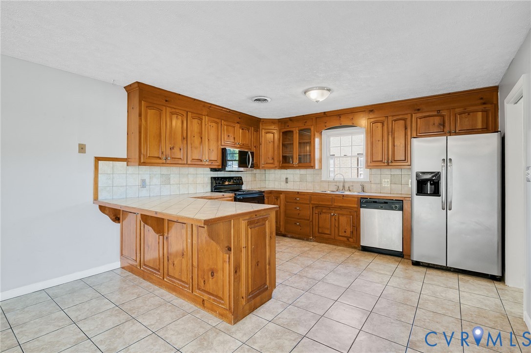 Kitchen featuring wood cabinetry, tile flooring, tile countertops, a tile backsplash, and stainless steel appliances