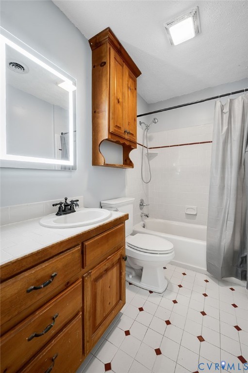 Vanity with wood-finish cabinetry, countertop with integrated sink, rectangular illuminated mirror, white tile flooring with accent squares, and a built-in bathtub with shower