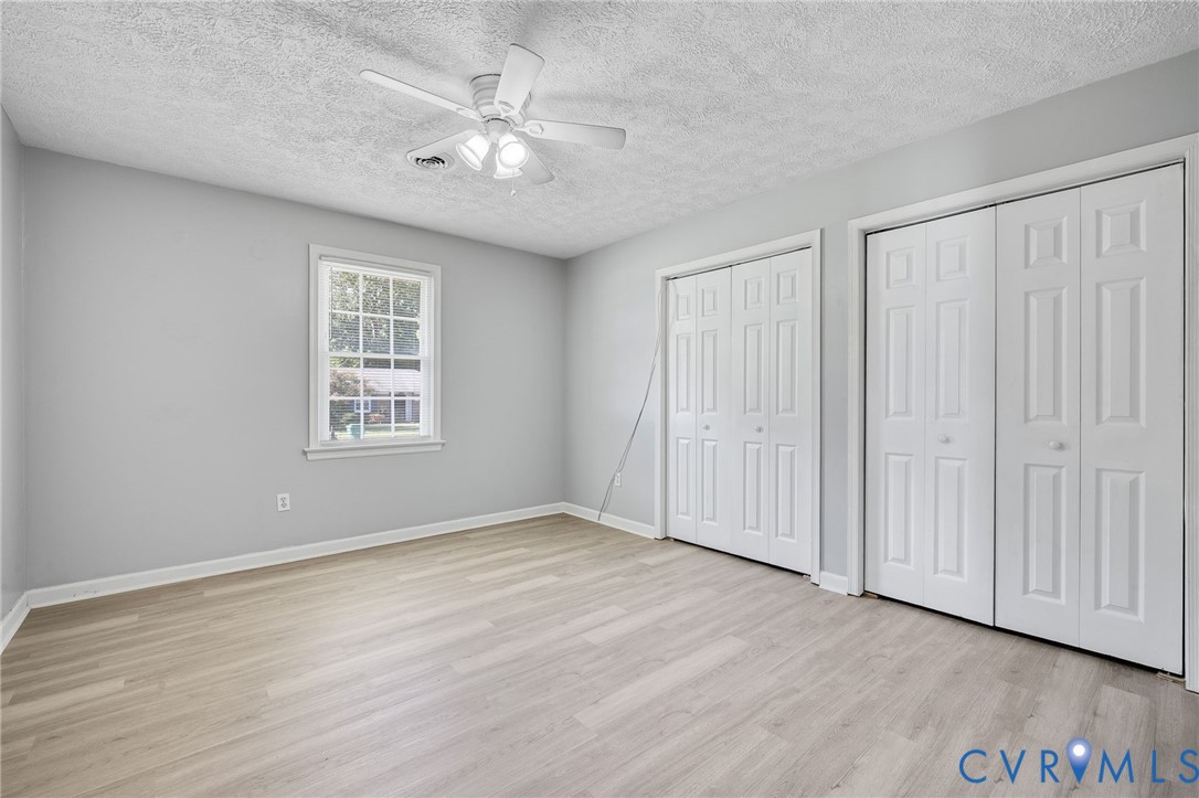 Wood-finish flooring, two sets of bi-fold closet doors, a single window, and a ceiling fan with light fixture