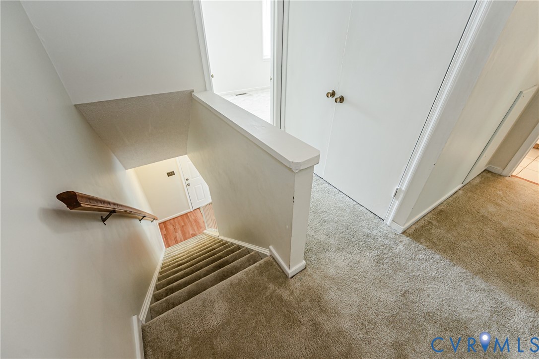 Carpeted staircase with a wood handrail leading to a lower level with wood-finish flooring