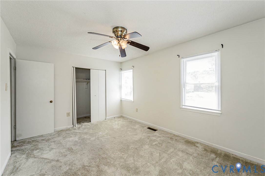 Carpeted interior room featuring a ceiling fan, two windows with blinds, a closet with bi-fold doors, and a door with a round doorknob
