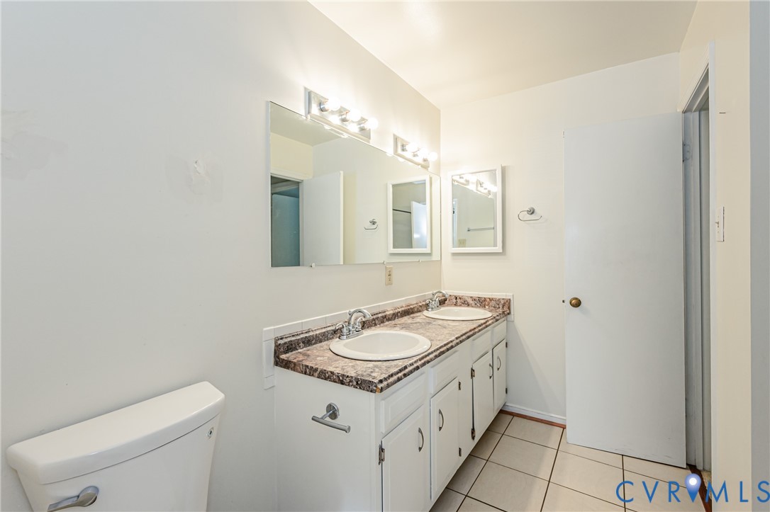 Bathroom featuring a dual vanity with a patterned countertop, two undermount sinks, and white cabinetry