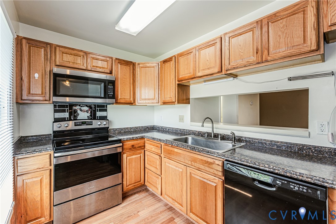 Kitchen featuring wood cabinetry, stainless steel over-the-range microwave, electric range, black dishwasher, and a double basin sink