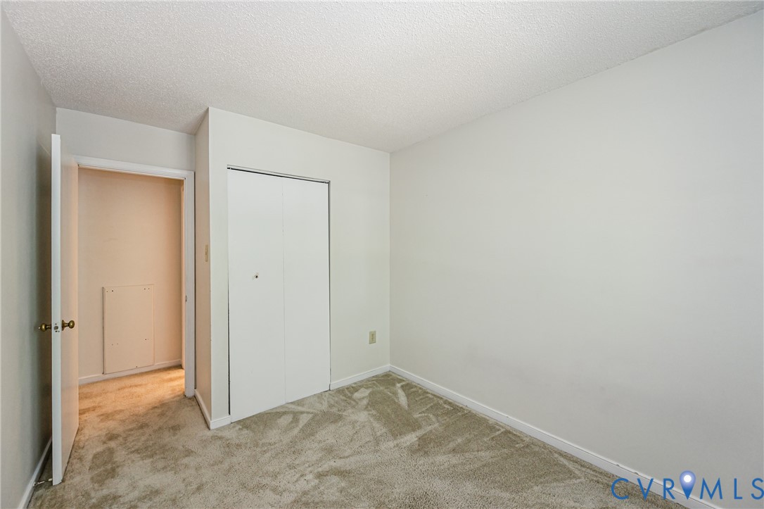 Carpeted room featuring white walls, a textured ceiling, a bi-fold closet door, and an open doorway