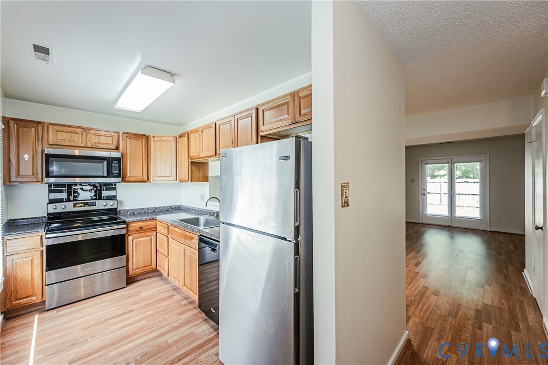 Kitchen featuring wood-finish flooring, stainless steel appliances, wood cabinetry, and granite-style countertops
