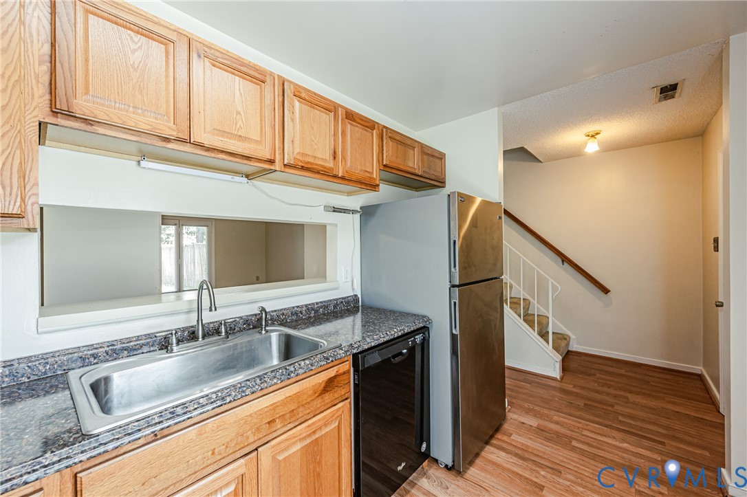 Kitchen featuring wood cabinetry, stainless steel sink with gooseneck faucet, dark granite-style countertops, and a pass-through window