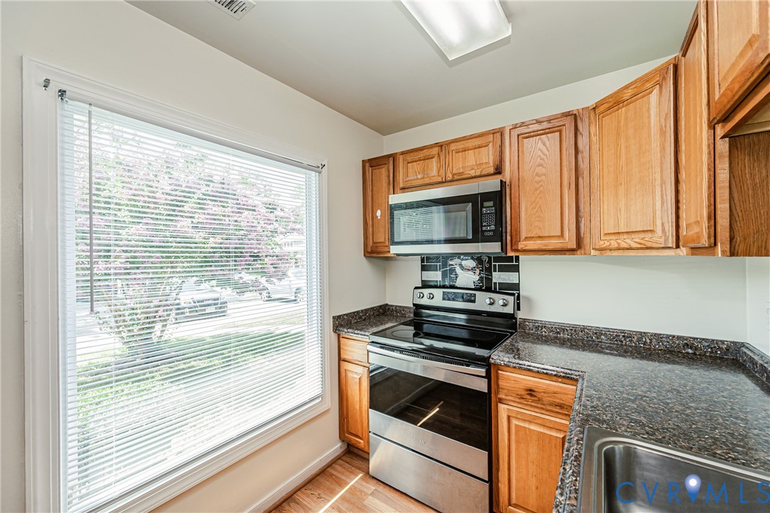 Kitchen featuring wood-finish cabinetry, stainless steel appliances, dark speckled countertops, and a tile backsplash
