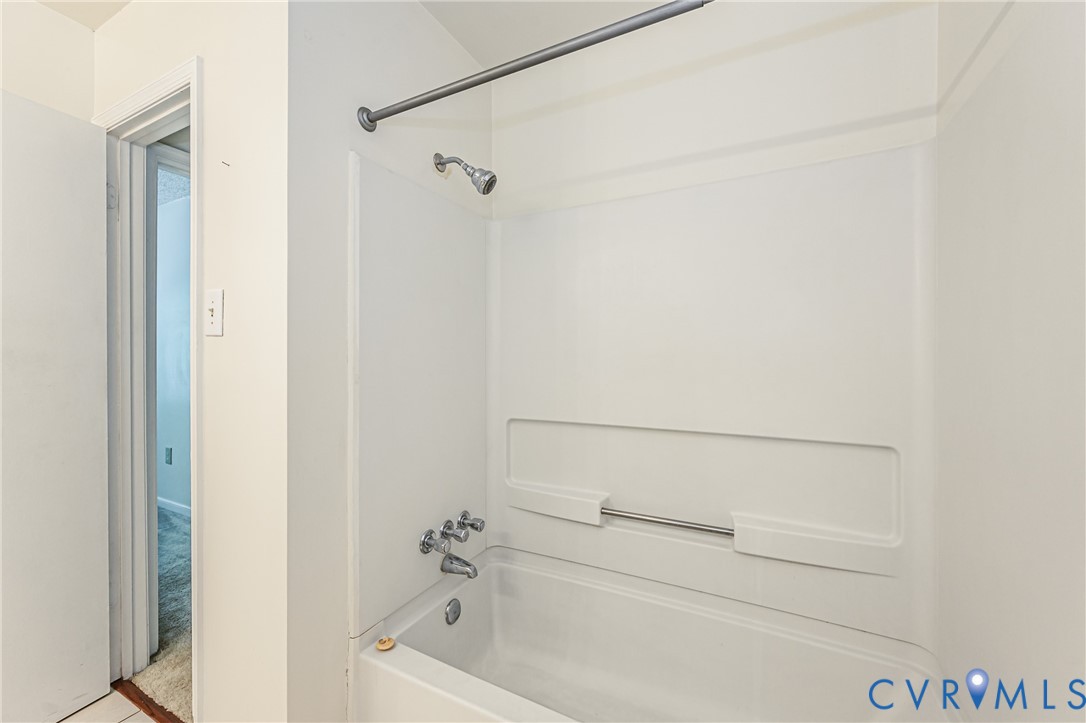 White bathtub and shower surround with chrome fixtures, including a shower head and dual-handle faucet