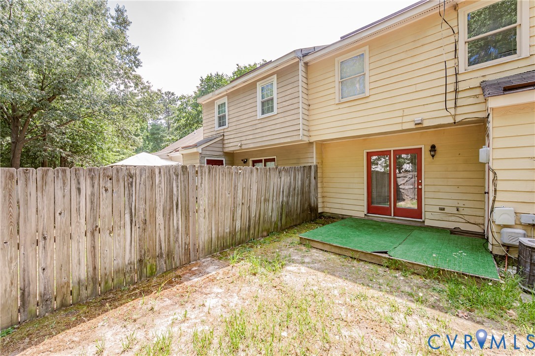 Rear exterior featuring yellow siding, red double glass doors, a small patio area with green turf, and a wood privacy fence