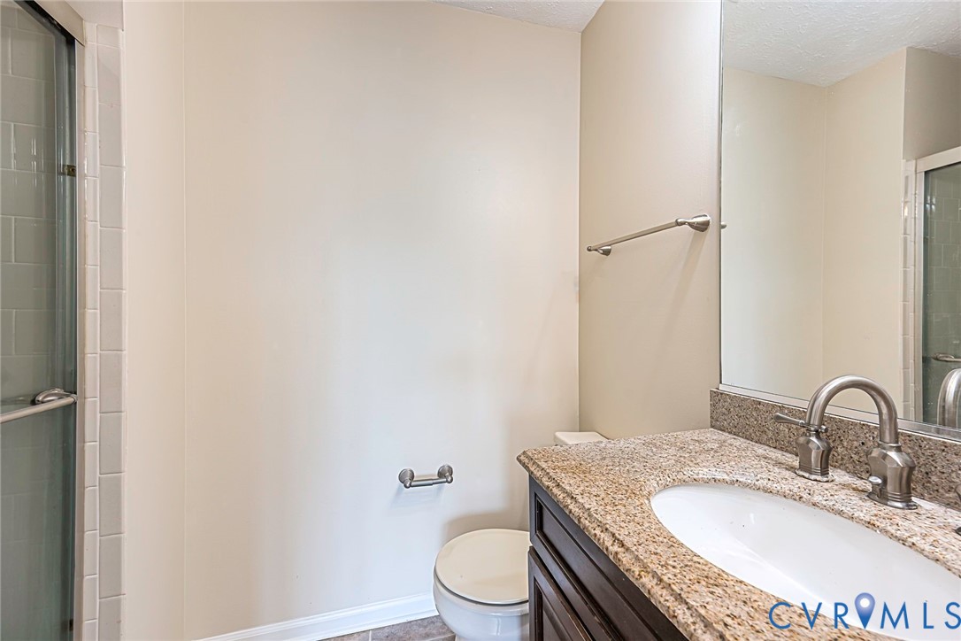 Bathroom featuring a granite countertop vanity with an undermount sink and brushed nickel faucet, a glass-enclosed shower, and neutral wall paint