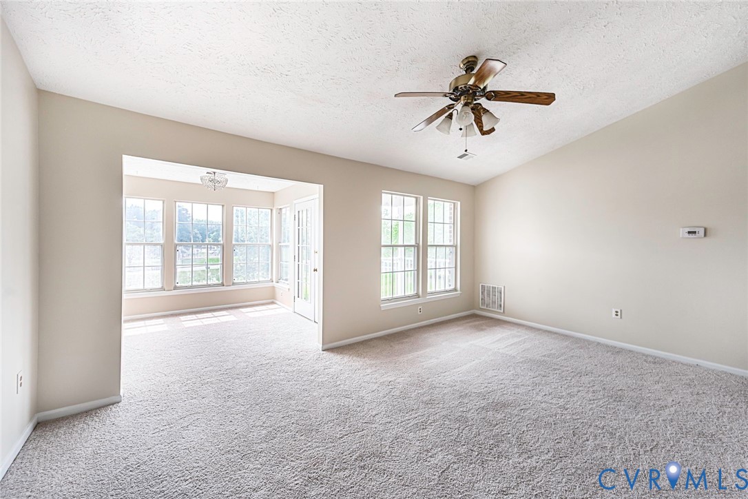 Vaulted ceiling with a ceiling fan, plush carpet flooring, and an adjoining sunroom with multiple windows and a glass-paneled door