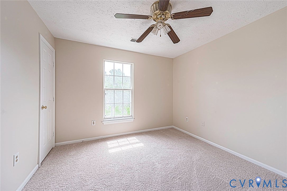 Neutral-toned room featuring a single window, light beige carpet, and a brass-finished ceiling fan with wood-finish blades