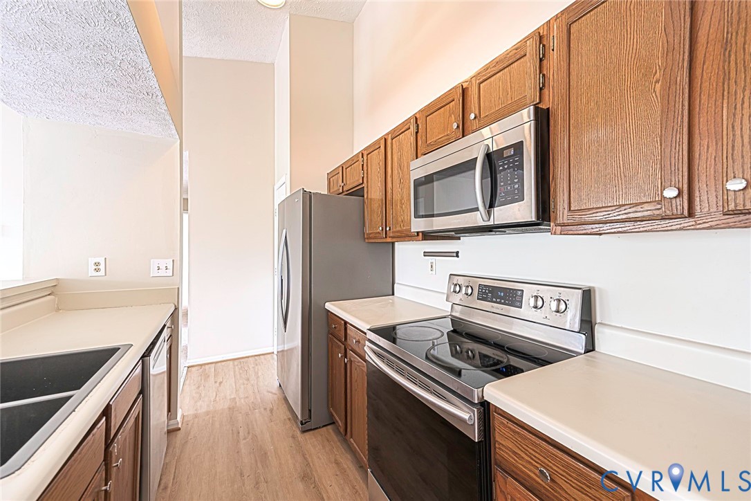 Kitchen featuring wood cabinetry, light-toned countertops, stainless steel appliances, and wood-finish flooring
