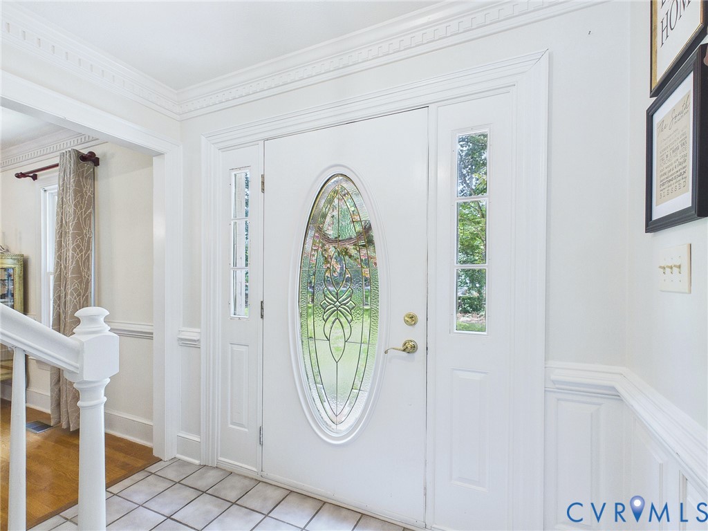 Entryway featuring a decorative oval-paneled door with sidelights, complemented by white wainscoting and crown molding
