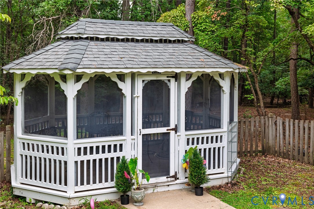 White screened gazebo featuring a tiered roof with grey shingles, decorative arch supports, and a slatted lower railing