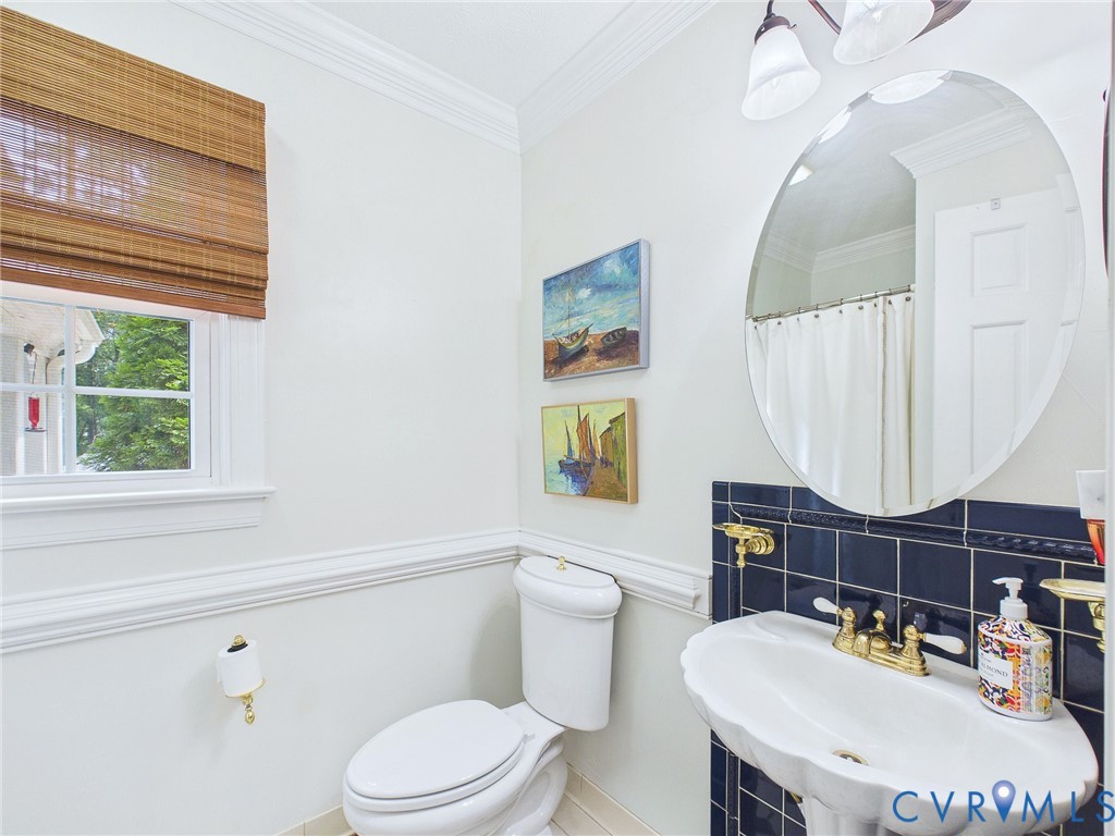 Bathroom featuring a pedestal sink with brass-finish fixtures, a dark tiled backsplash, and an oval wall mirror