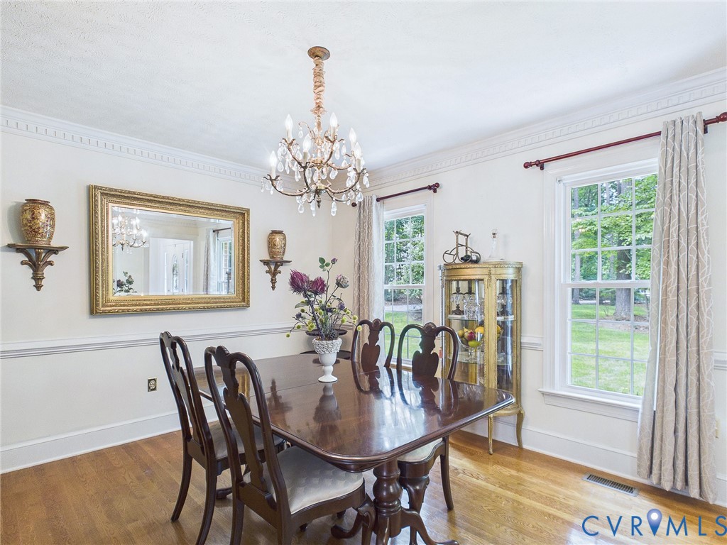 Dining area featuring hardwood flooring, a crystal chandelier, crown molding, and large windows with natural light
