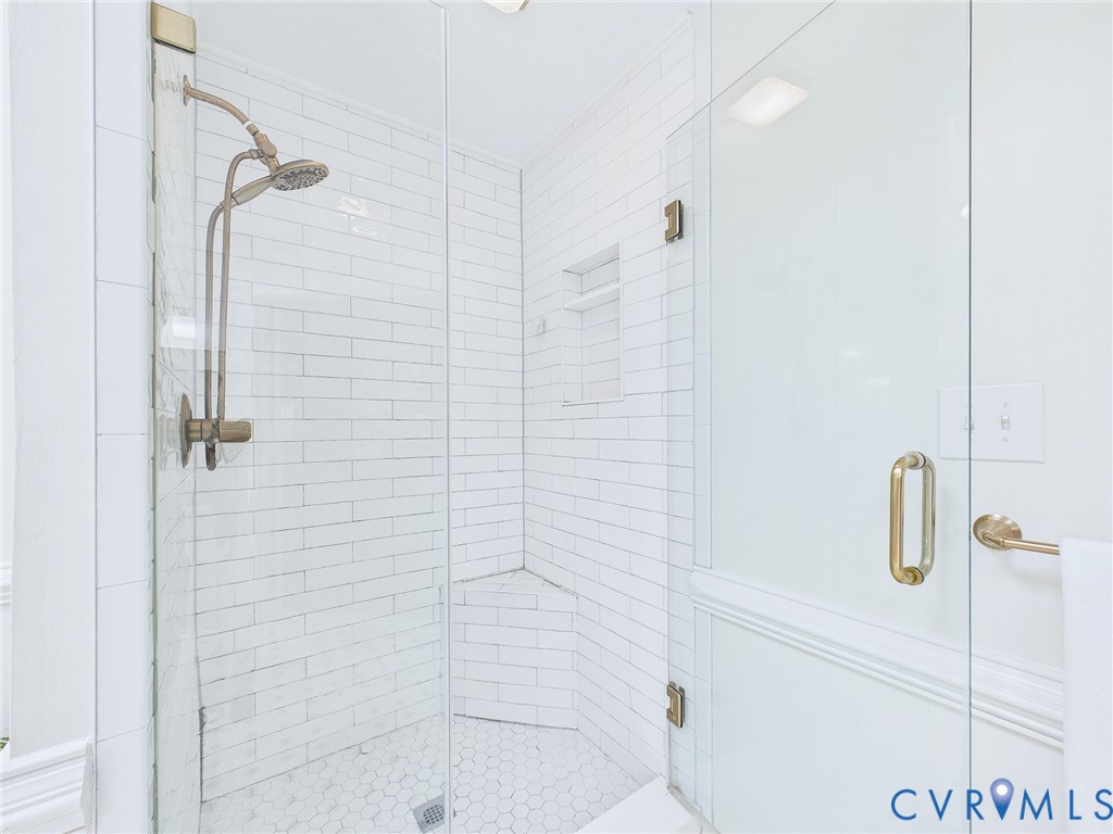 Glass-enclosed shower featuring white subway tile walls, a built-in shower niche, and a hexagon tile floor