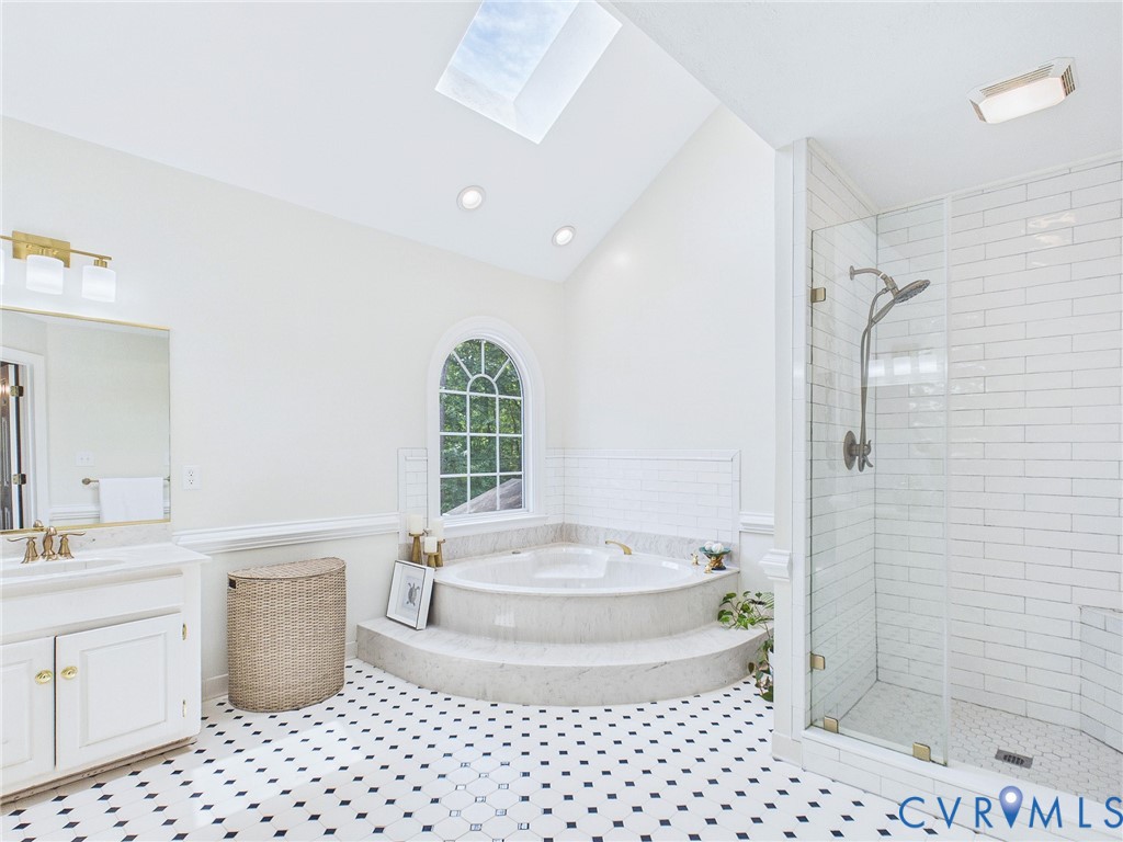 Bathroom featuring a built-in jetted tub with tiled surround, a separate glass-enclosed shower, a double vanity with a marble-finish countertop, and black and white patterned floor tiling