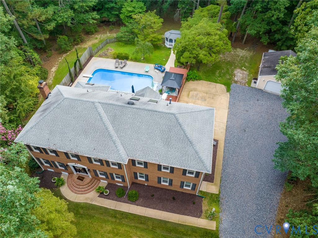 Two-story brick residence featuring a gray shingle roof, a fenced backyard with an in-ground swimming pool, a detached garage, and a gravel driveway Two-story brick residence featuring a gray shingle roof, a fenced backyard with an in-ground swimming pool, a detached garage, and a gravel driveway