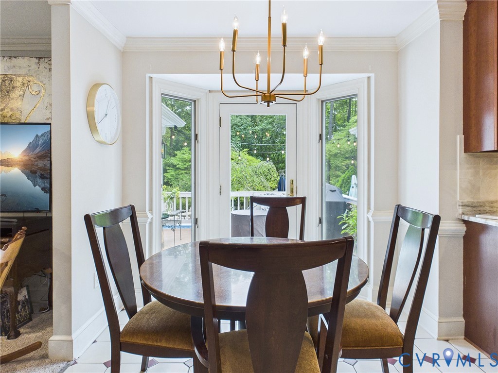 Dining area featuring a brass chandelier, a bay window with multiple glass-paned doors, crown molding, and a tiled floor with a geometric pattern