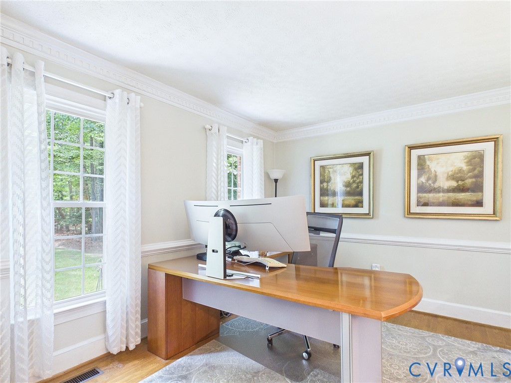 Room featuring crown molding, chair rail molding, multiple windows, wood-finish flooring, and a patterned area rug