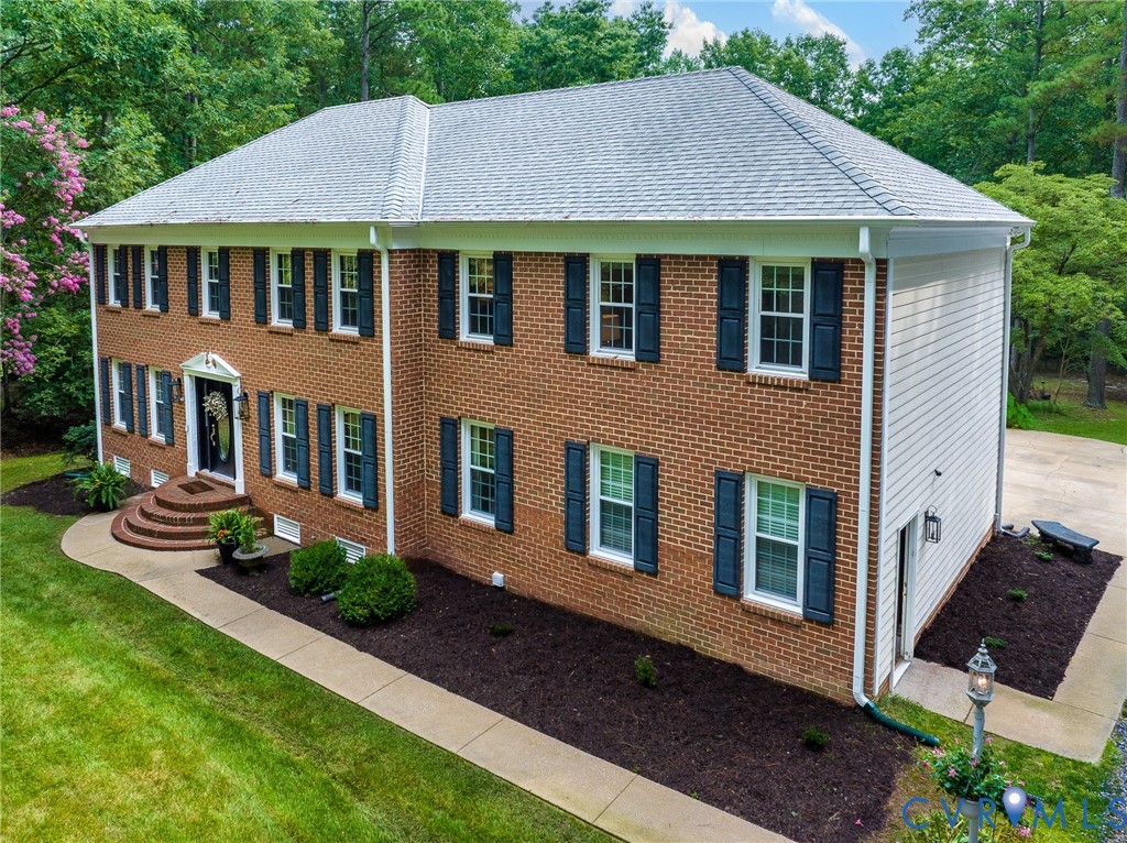 Traditional two-story brick residence featuring a gray shingle roof and white gutters Traditional two-story brick residence featuring a gray shingle roof and white gutters