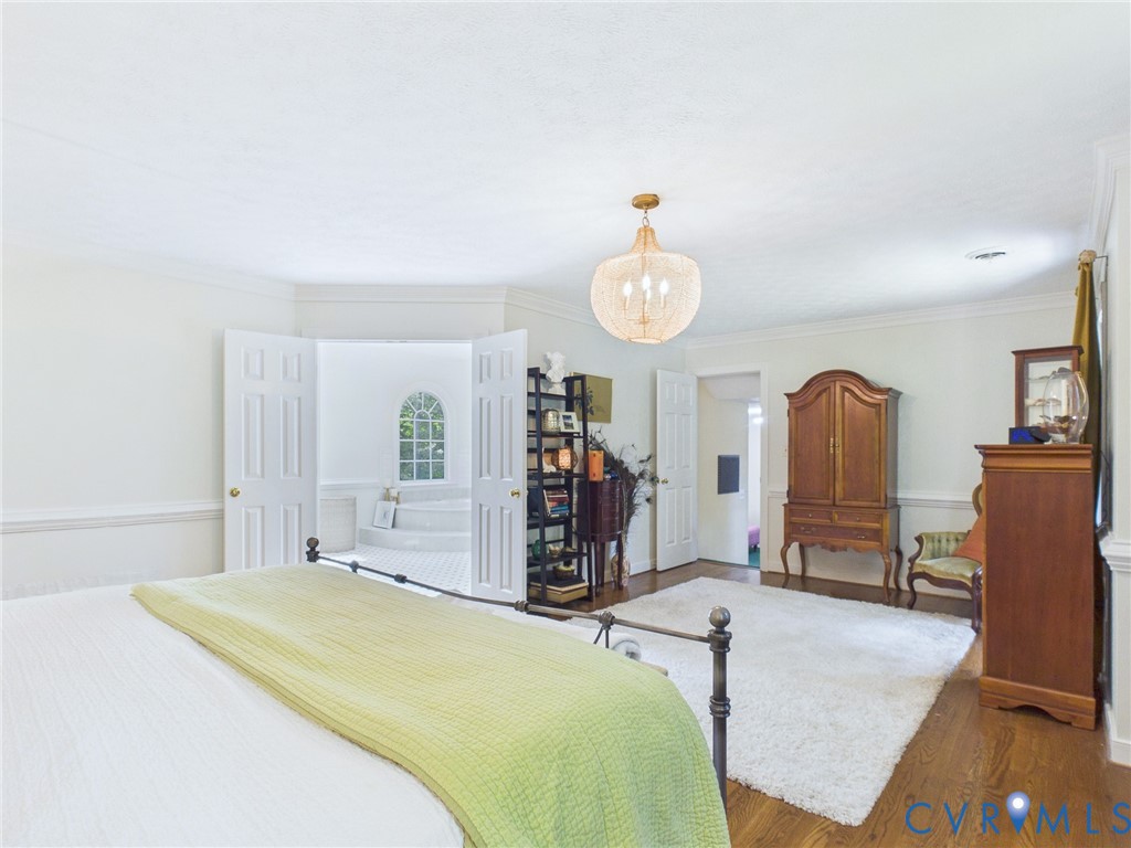 Spacious room featuring hardwood flooring, crown molding, and a prominent chandelier