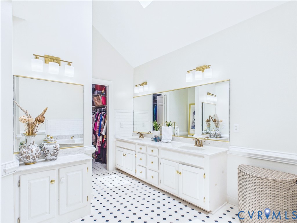 Vaulted ceiling bathroom featuring dual vanities with white cabinetry and gold-tone hardware