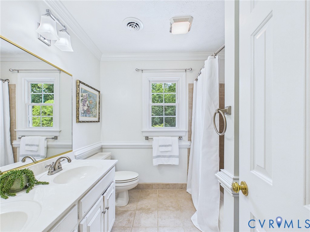 Bathroom featuring a dual-sink vanity with white cabinetry, a toilet, two windows, and a shower area with a curtain