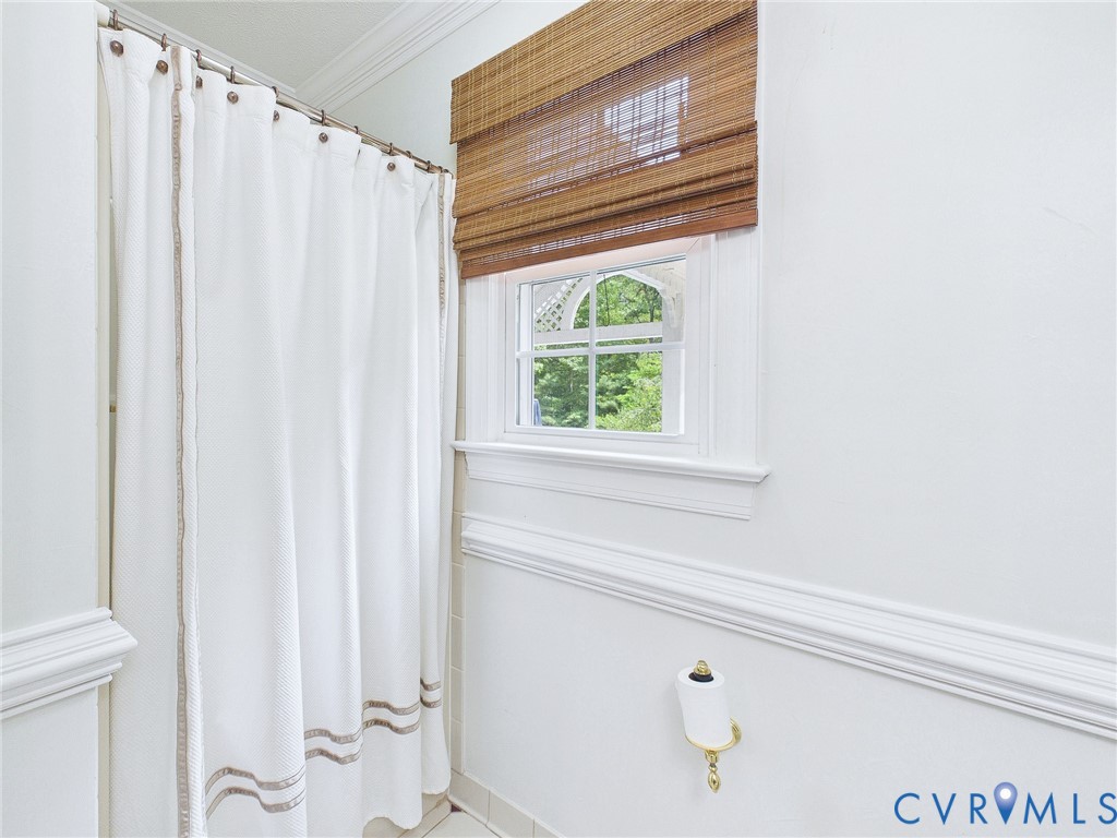 Bathroom featuring a window with an arched transom, woven wood shade, and extensive white molding