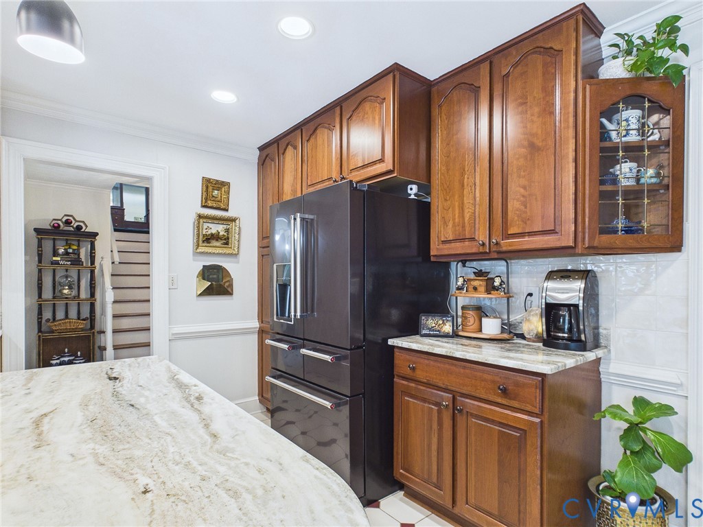 Kitchen featuring a large central island with a light-toned, variegated stone countertop, floor-to-ceiling wood cabinetry, a built-in refrigerator, and a tiled backsplash
