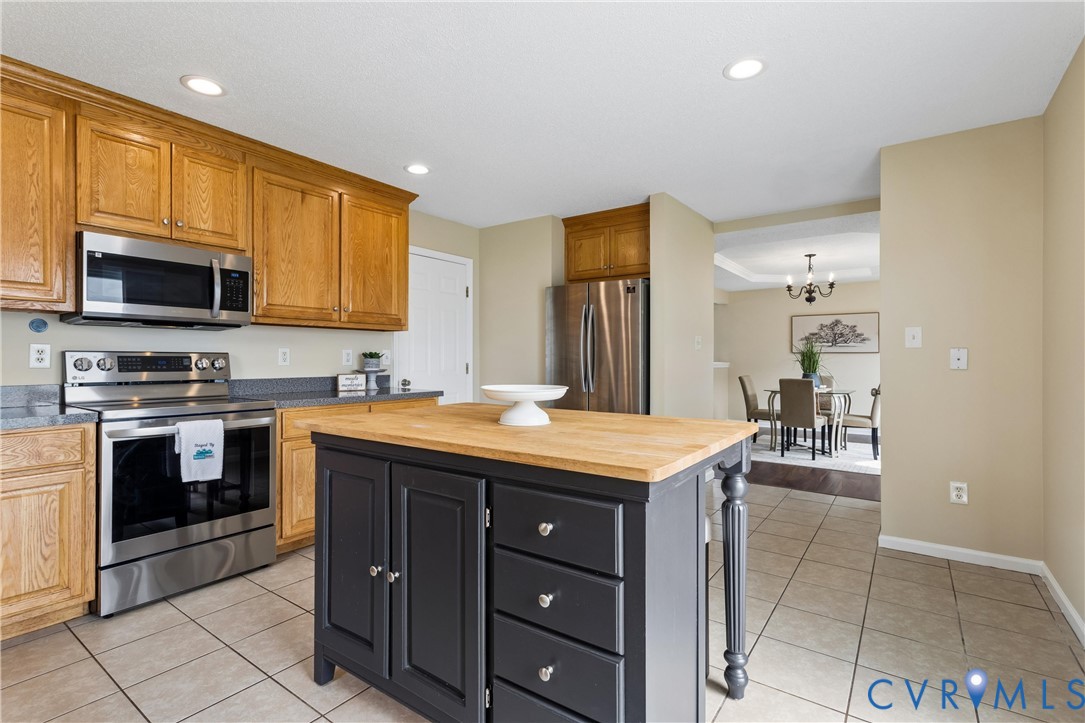 Kitchen featuring a central island with a wood-finish countertop, stainless steel appliances, wood-finish cabinetry, recessed lighting, and tile flooring