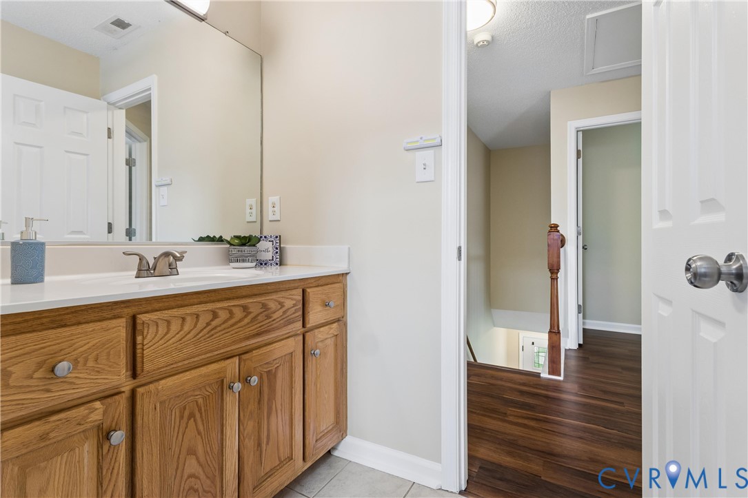 Bathroom vanity with a white countertop and integrated sink, featuring wood-finish cabinetry, a large wall-mounted mirror, and tile flooring