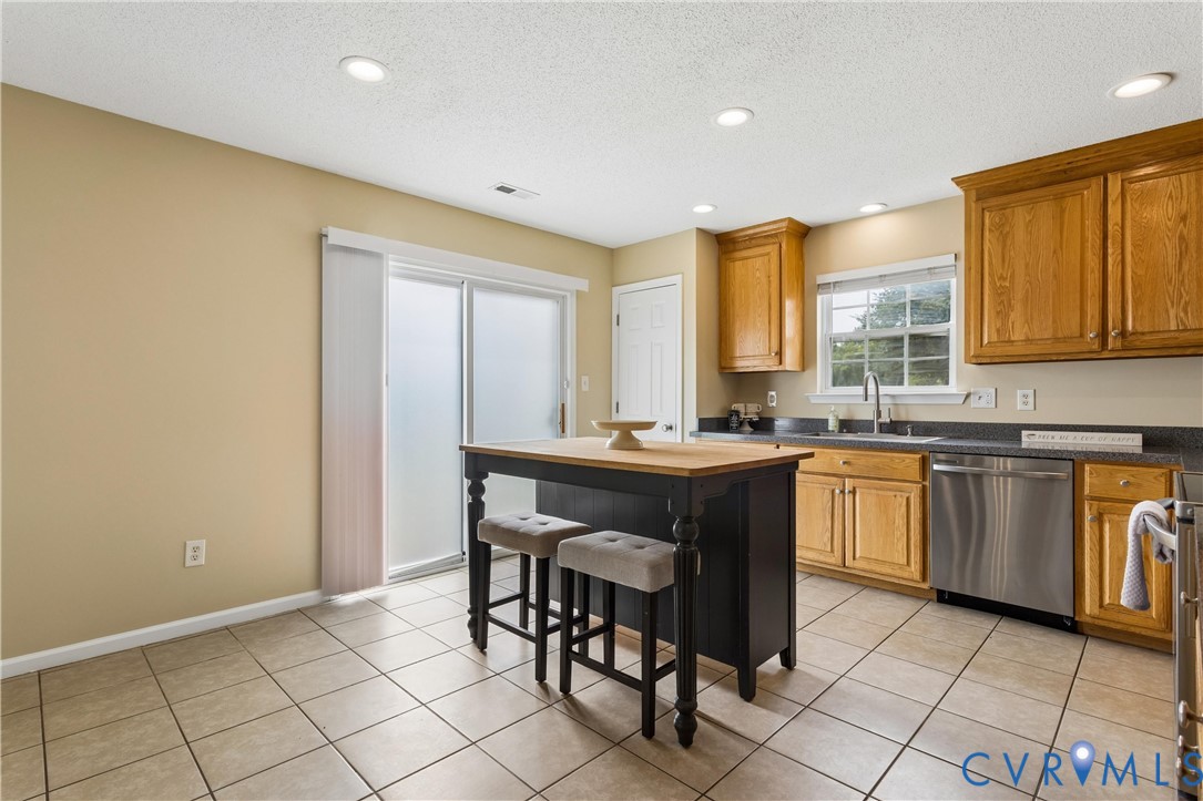 Kitchen featuring a central island with a wood-finish countertop, tile flooring, wood cabinetry, stainless steel dishwasher, and recessed lighting