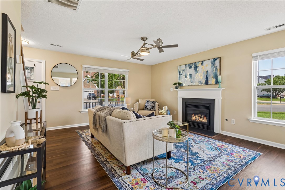 Living area with wood-finish flooring, a white mantel fireplace, and ample natural light from multiple windows Living area with wood-finish flooring, a white mantel fireplace, and ample natural light from multiple windows