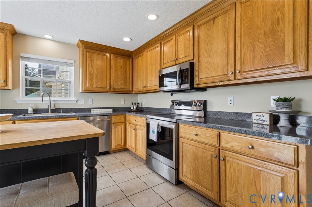 Kitchen featuring wood cabinetry, stainless steel appliances, dark countertops, and tile flooring