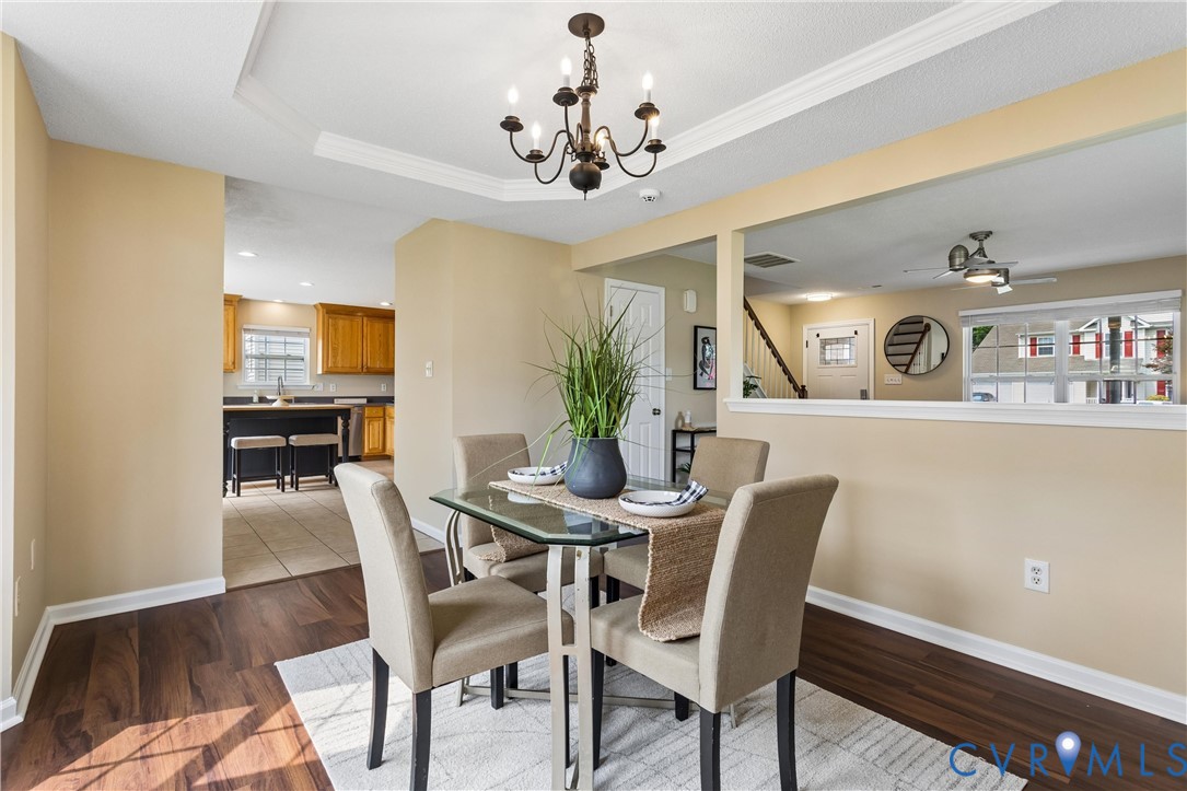 Dining area featuring wood-finish flooring and a tray ceiling with a dark-finish chandelier Dining area featuring wood-finish flooring and a tray ceiling with a dark-finish chandelier