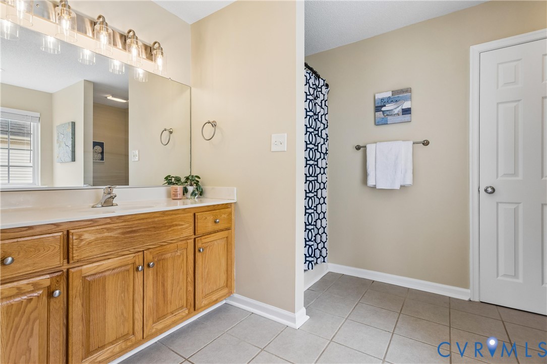 Bathroom featuring a wood-finish vanity with a single sink and light-toned countertop, a large wall-mounted mirror, and a multi-bulb vanity light fixture