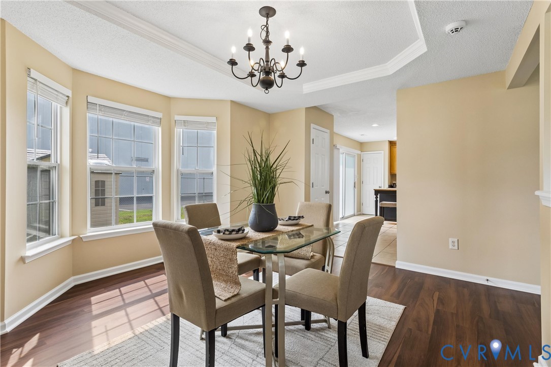 Dining area featuring a bay window with multiple panes, wood-finish flooring, a tray ceiling detail, and an overhead chandelier Dining area featuring a bay window with multiple panes, wood-finish flooring, a tray ceiling detail, and an overhead chandelier